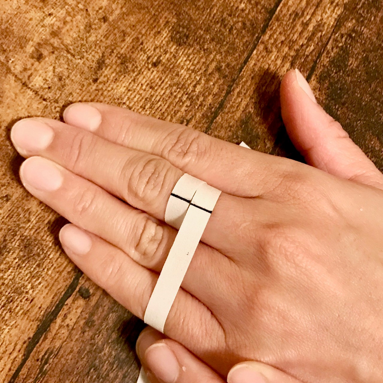 <p>測定したい指の一番太い部分（第2関節より少し下辺り）にヒモ、又は紙を巻き付けます。※この時のフィット感が指輪をはめた時の感覚に近いです。円周1mmの違いで1サイズぐらいの差が出ますので、ゆるくならないように注意して巻き付け具合を調節しましょう。一周巻き付けて重なった部分にペンで目印を付けます。<br>※見やすいように少し太めのヒモを使用し、太めの印を付けています。